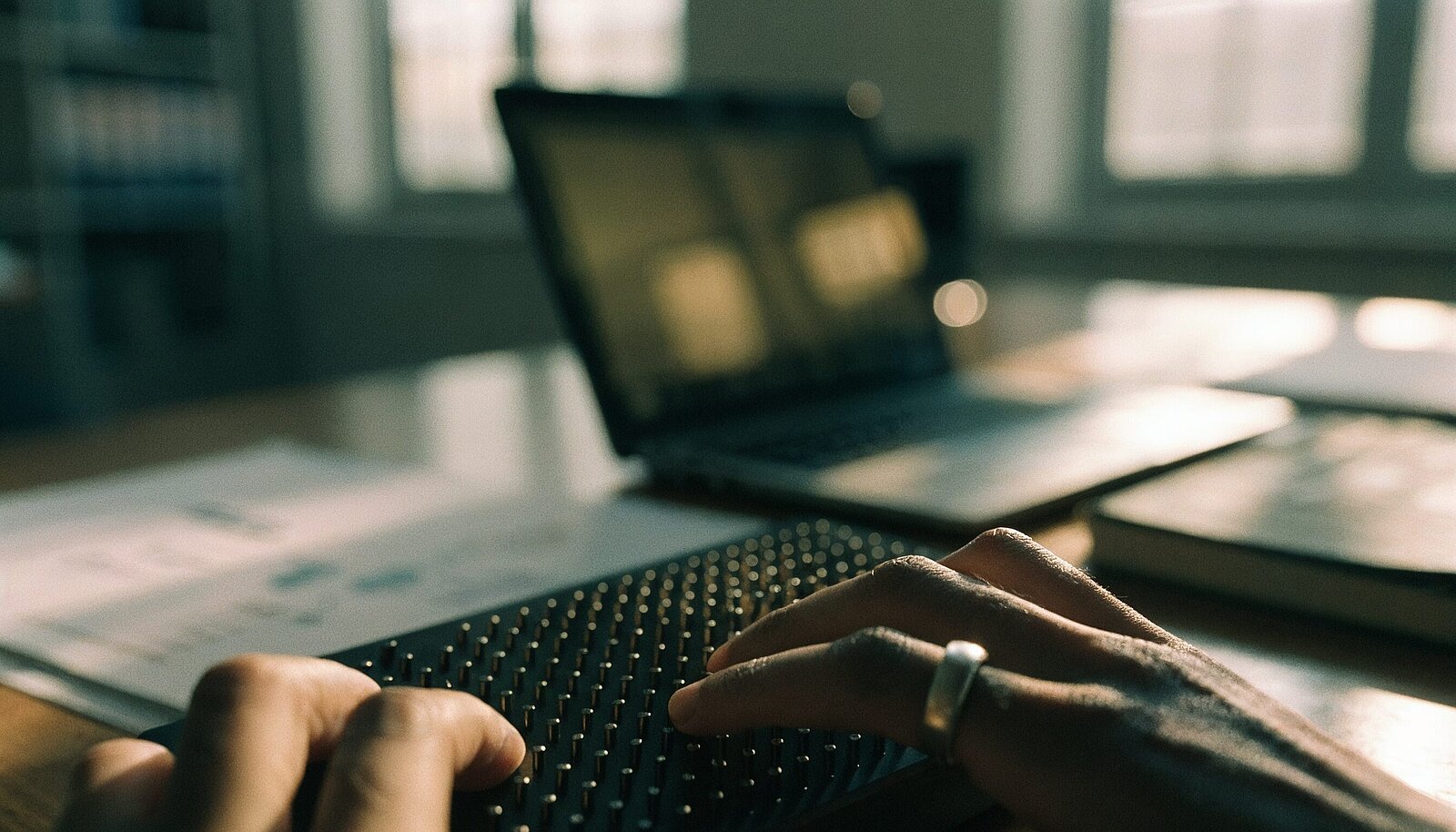 Fingerspitzen lesen eine Braillezeile vor einem unscharfen Laptop